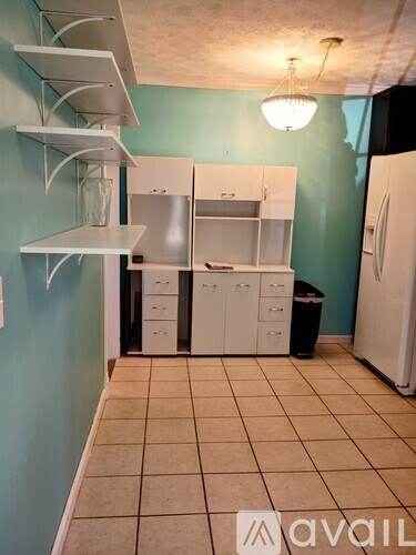 A kitchen with a white fridge, white cabinets, and a black trash can.