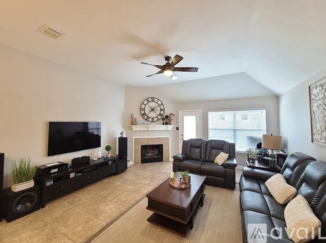 A living room with a fireplace, two couches, a television, and a ceiling fan.