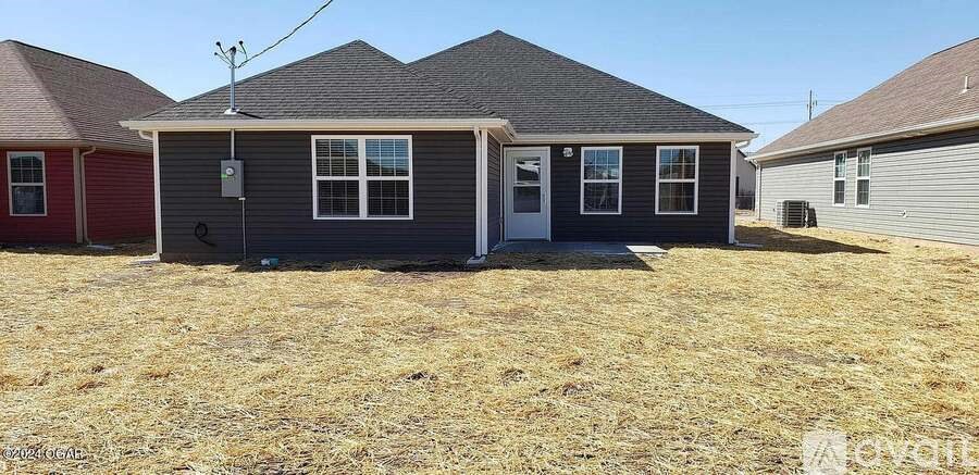 A grey house with a red door is situated in a grassy area.