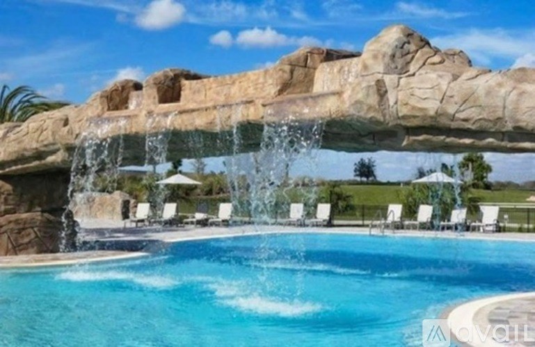 A large rock arch with water flowing over it into a pool.