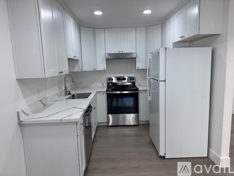A white kitchen with a refrigerator, stove, and sink.