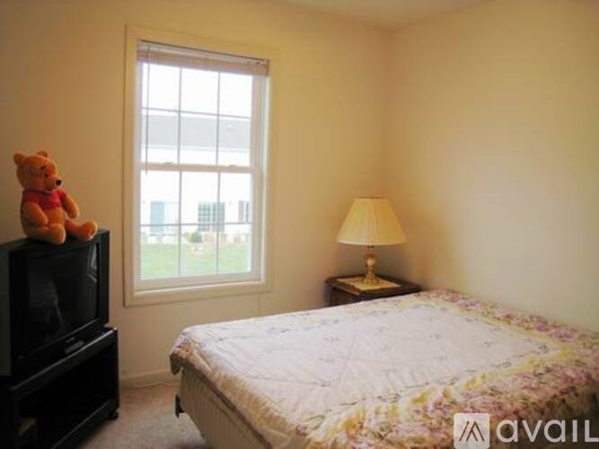 A bedroom with a bed, a television, a window, and a lamp.