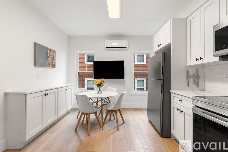 A modern dining room with a white table and chairs, a television, and a painting on the wall.