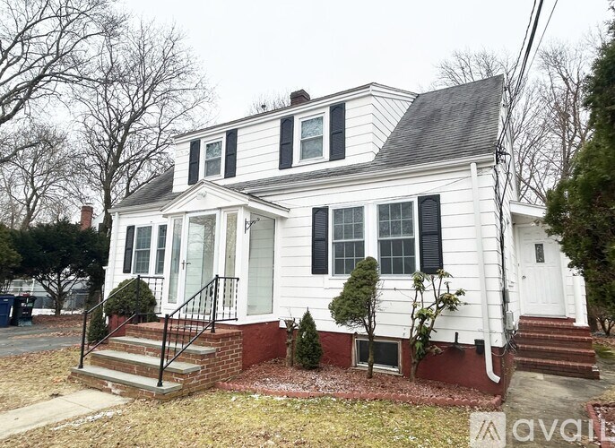 A white house with a black roof and a red brick foundation.