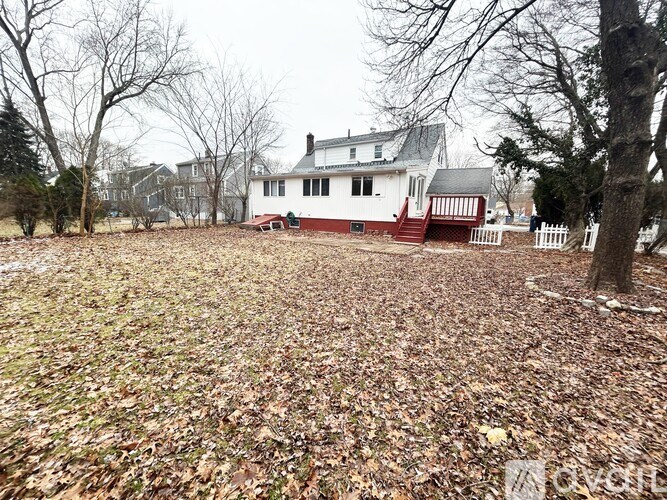 A white house with a red roof is surrounded by trees and a field of leaves.