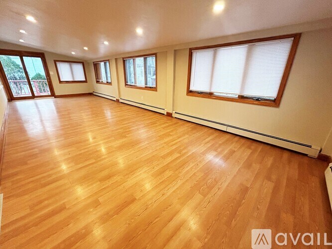 A spacious room with wooden flooring and large windows.