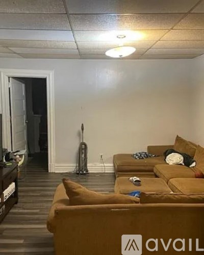 A living room with a brown couch and a vacuum cleaner in the background.