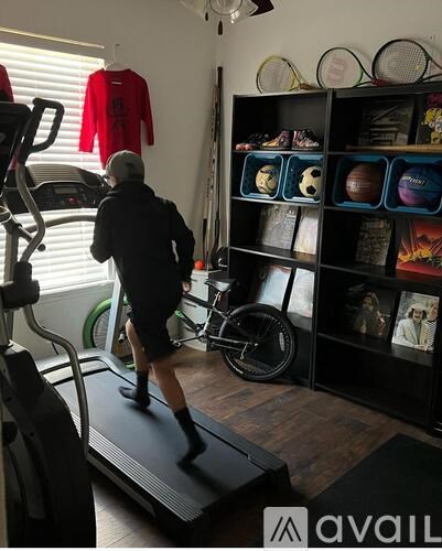 A man is running on a treadmill in a room with exercise equipment and a rack of tennis balls.