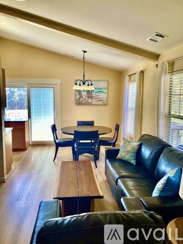 A living room with a black leather couch and a wooden table.