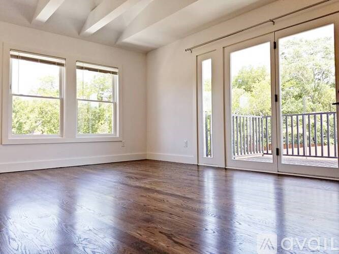 A spacious room with wooden floors and sliding glass doors leading to a balcony.