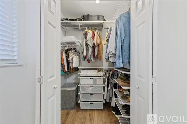 A small closet with clothes hanging and boxes on the floor.