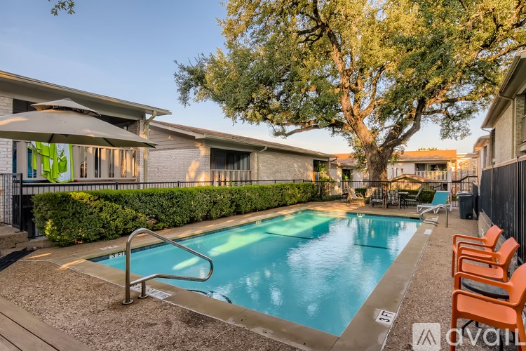 A pool surrounded by orange chairs and a tree.