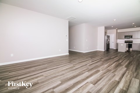 A spacious room with wooden flooring and a kitchen area in the background.
