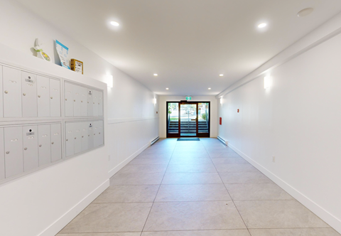 A long hallway with white walls and a row of lockers on the left side.