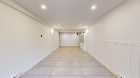 A long, empty hallway with white walls and tiled flooring.