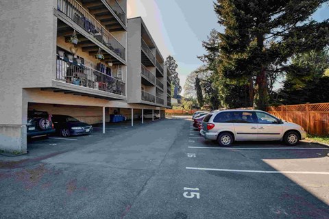 A parking lot with cars parked and a building with balconies in the background.