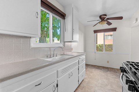 A kitchen with white cabinets and a brown ceiling fan.