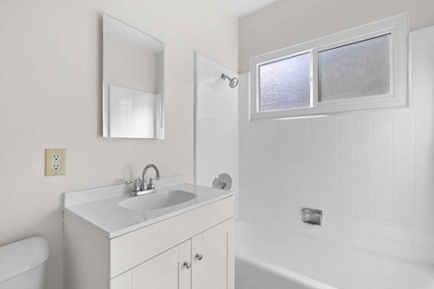 A white bathroom with a sink, mirror, and bathtub.