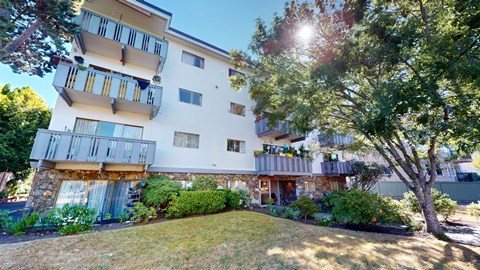 A white apartment building with balconies and trees in front.