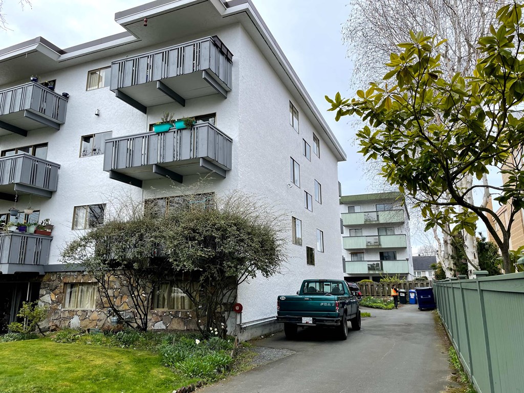 A white apartment building with balconies and a green truck parked in front.
