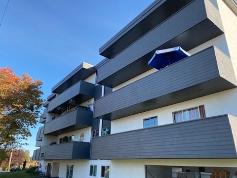 A modern apartment building with balconies and a blue awning.