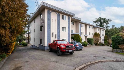 A red car is parked in front of a white building with blue trim.