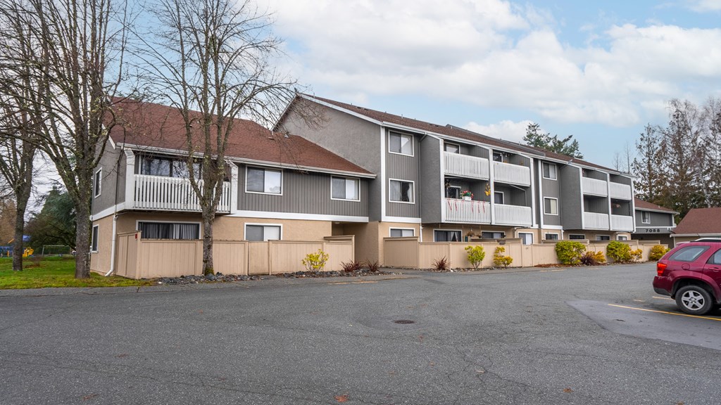 A red car is parked in the parking lot in front of a building.
