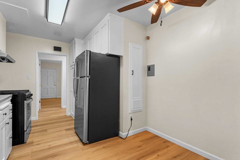 A black refrigerator in a kitchen with wooden floors and white walls.