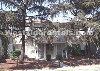 A white house with a porch and a tree in front.