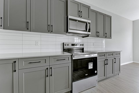 A kitchen with grey cabinets and a black oven.