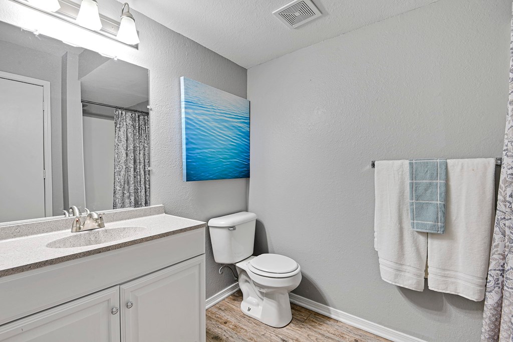 A bathroom with a toilet, sink, and a painting on the wall.