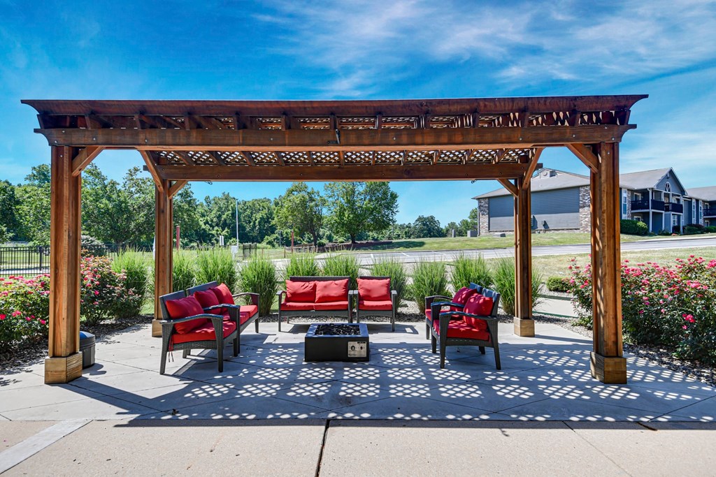 A wooden pergola with red cushioned chairs and a black box underneath it.