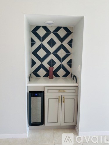 A kitchen with a black and white tiled wall and a white cabinet with a black fridge.