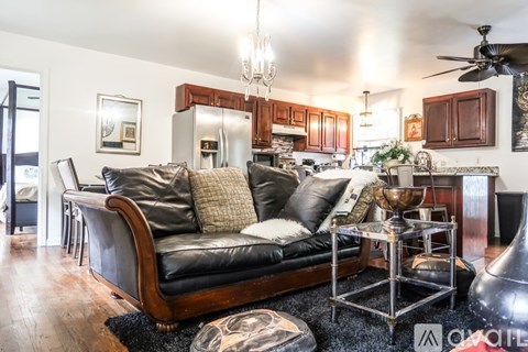 A living room with a black leather couch and a chandelier.