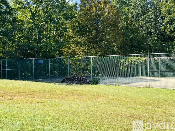 A chain link fence separates a grassy field from a wooded area.