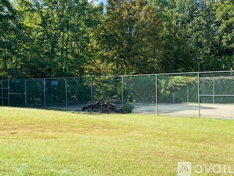 A chain link fence separates a grassy field from a wooded area.