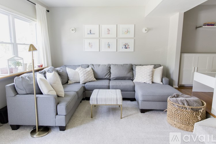 A grey sectional sofa with a white pillow and a white ottoman in front of it.