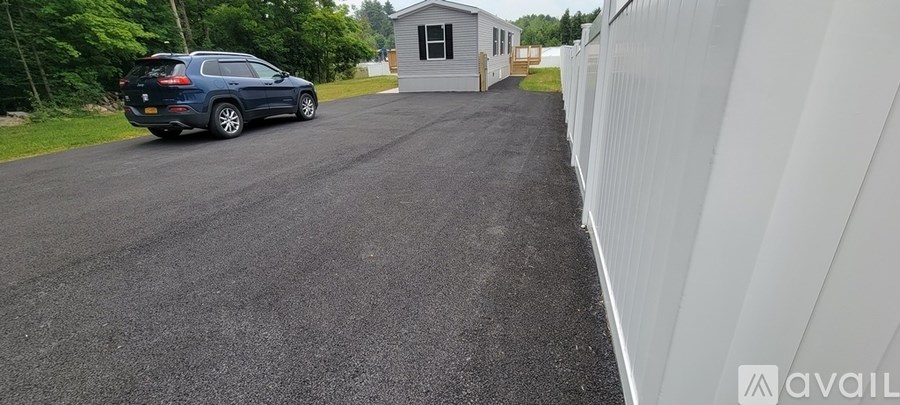 A car is parked on a driveway next to a white fence.