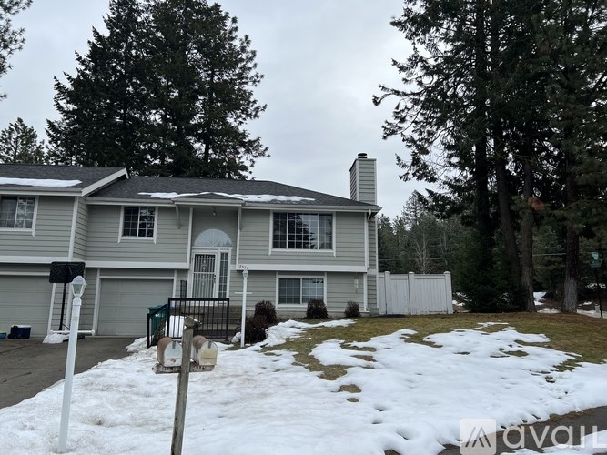 A house with a grey roof and a white fence is surrounded by snow.