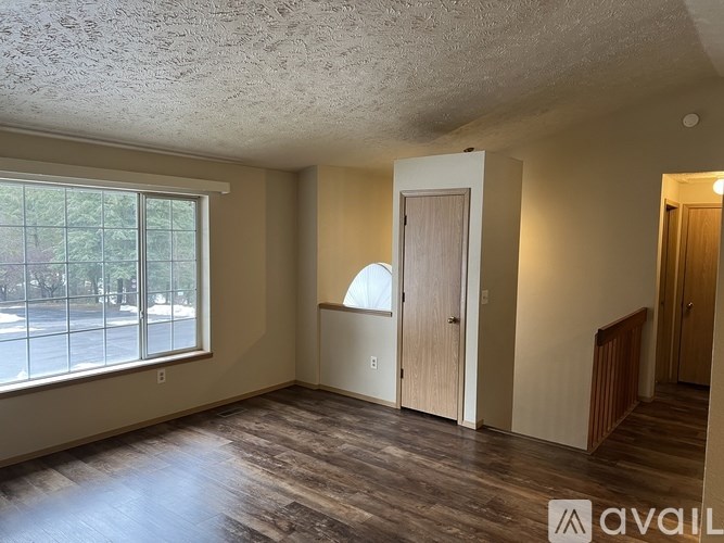 A room with wooden floors and a large window overlooking a parking lot.