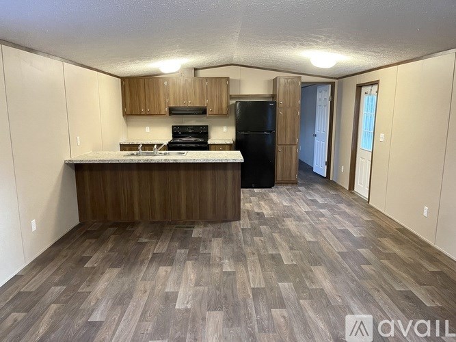 A kitchen with wooden flooring and a black refrigerator.