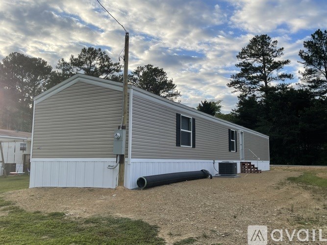 A mobile home with a grey siding and a white trim is situated in a grassy area with trees in the background.