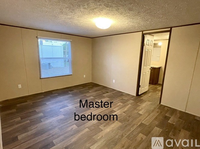 A master bedroom with wood flooring and a window with blinds.