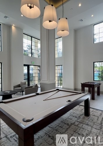 A pool table is in the middle of a room with a carpet and a couple of chairs.