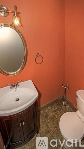 A bathroom with orange walls has a toilet, sink, and mirror.