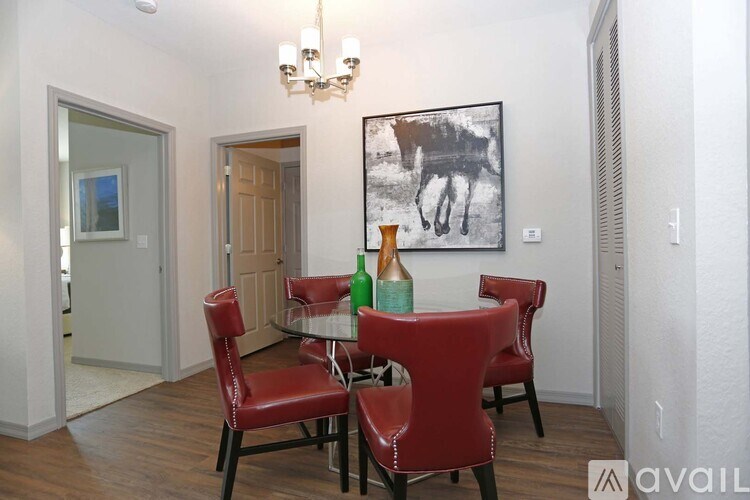 A dining room with a chandelier, a painting of a horse, and a table with red chairs.