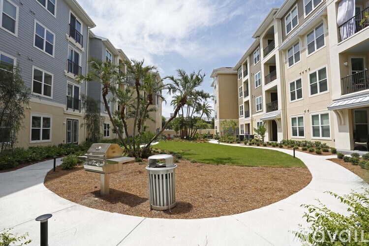 A roundabout with a trash can and bench in the middle of a courtyard between two apartment buildings.