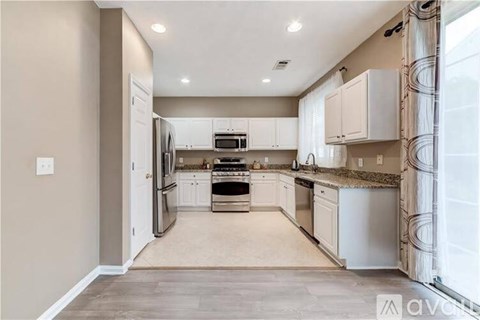 A kitchen with white cabinets and appliances, and a beige wall.