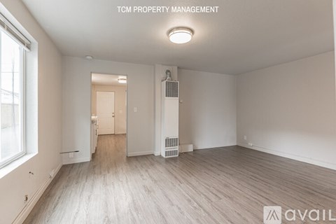 A spacious room with wood flooring and a window on the left side.
