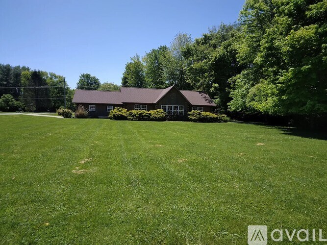 A house with a brown roof is surrounded by a green lawn and trees.